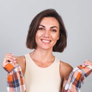 Beautiful woman in top and plaid shirt on gray background with makeup  positive confident smile, happy emotions