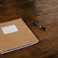 Craft brown folder with empty white label and a ballpoint pen on a rustic dark brown table