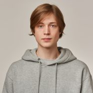 Serious looking male, handsome guy with blond hair. Wearing grey hoodie. People and emotion concept. Watching confident at the camera isolated over grey background
